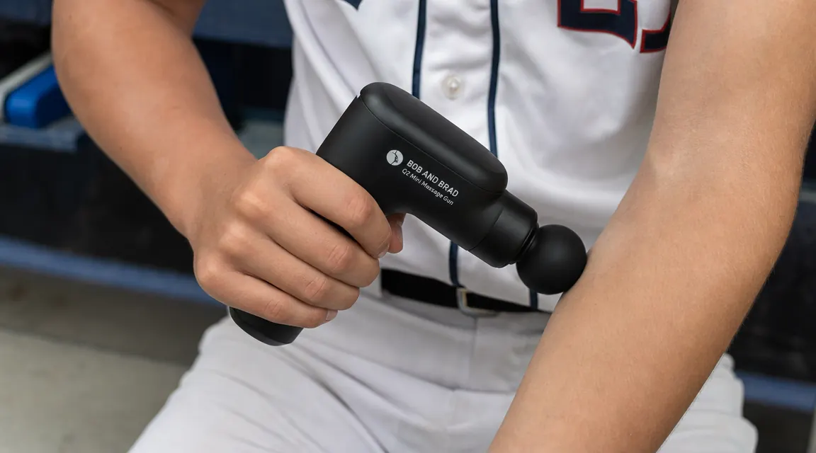 Close-up of a hand holding the BOB AND BRAD Q2 mini massage gun against a pitcher's forearm flexors
