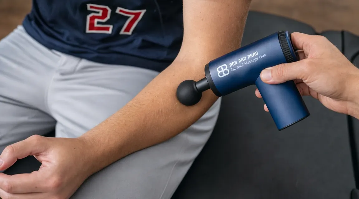 Hand holding the BOB AND BRAD Q2 massage gun and pressing the ball attachment against a pitcher's forearm flexor muscles