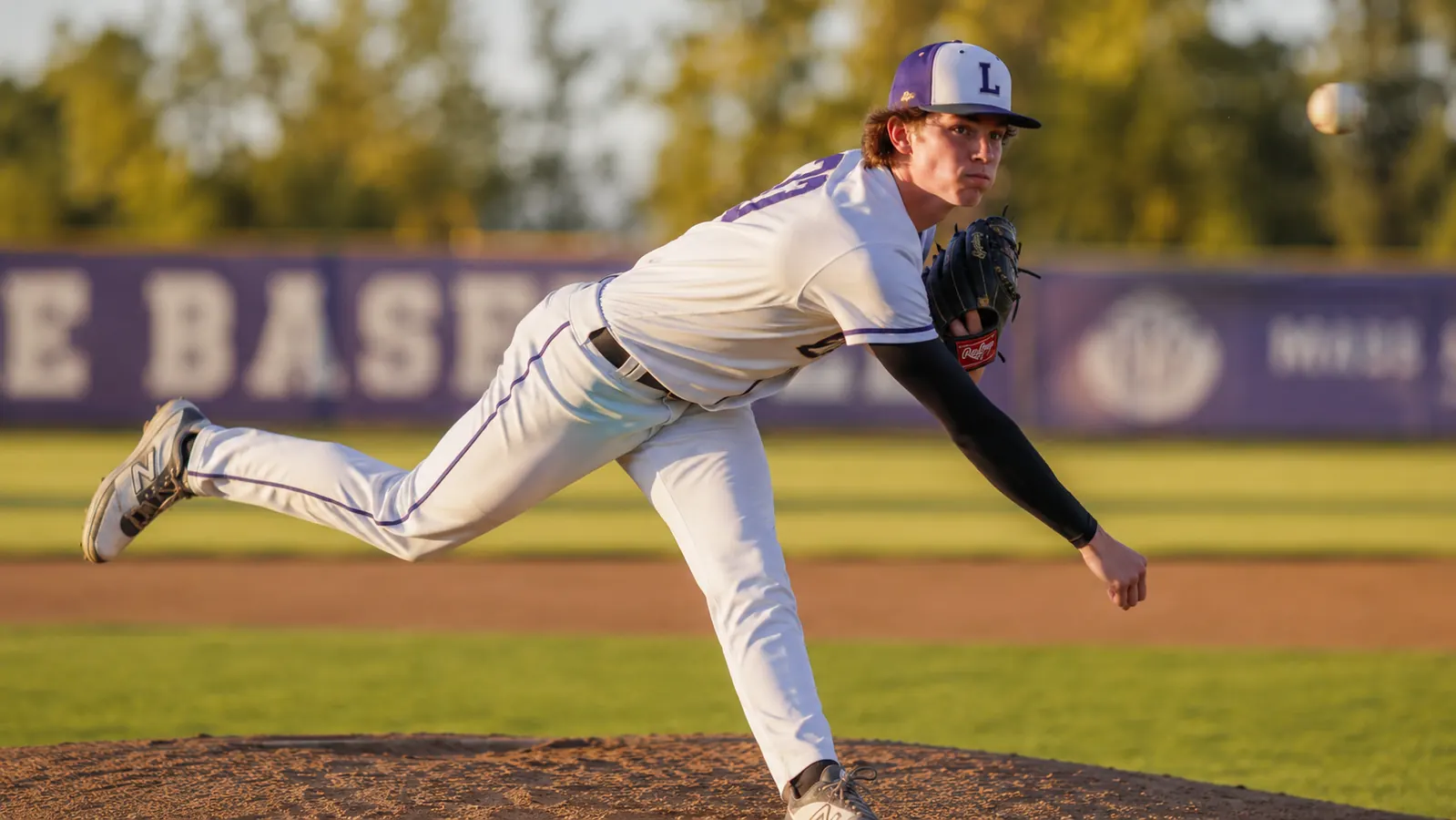 Teen pitcher on the mound mid-delivery, compression sleeve clearly visible on throwing arm under jersey