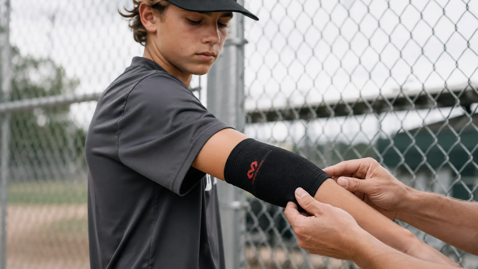 Close-up of the McDavid Elastic Elbow Support being fitted onto a teen pitcher's forearm
