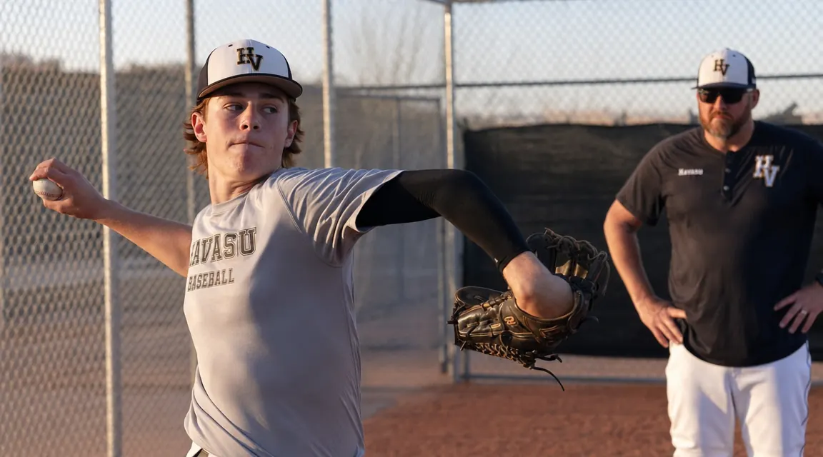 Teen pitcher warming up in the bullpen wearing a compression elbow sleeve under his jersey, coach standing nearby
