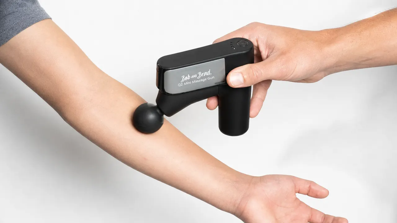 Compact BOB AND BRAD Q2 mini massage gun being held against a pitcher's forearm flexor muscles