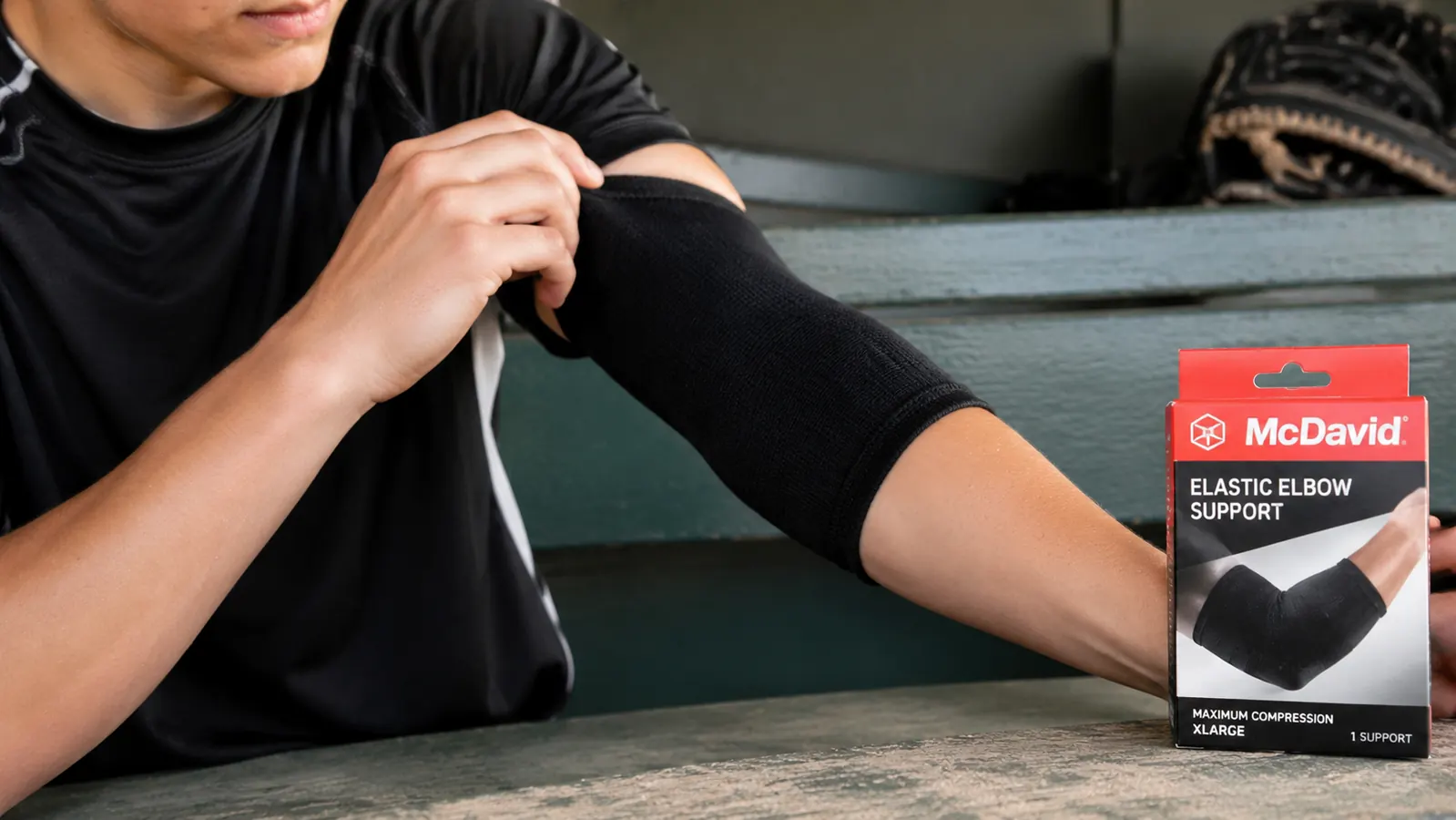 Close-up of the McDavid elastic elbow support being pulled onto a teen athlete's arm in a dugout