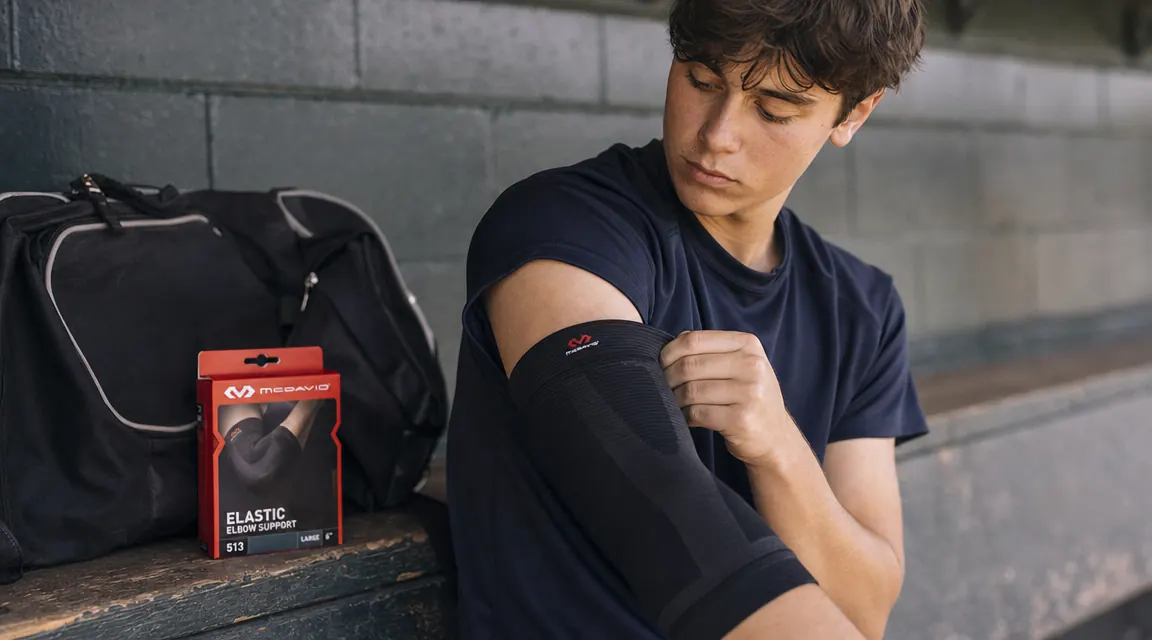 McDavid elastic elbow support being pulled onto a teenage pitcher's arm before a practice session